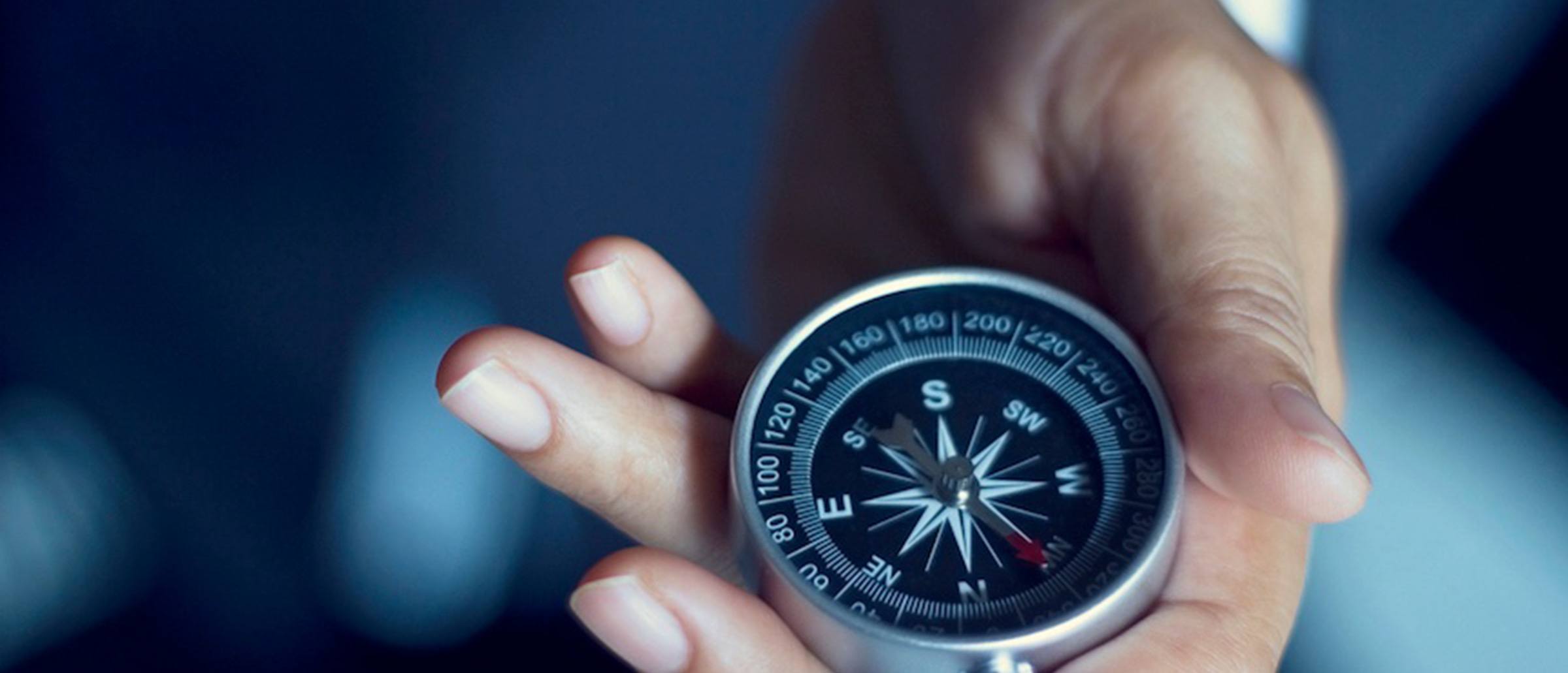 A hand holding a grey, black and white compass with pointed red arrow